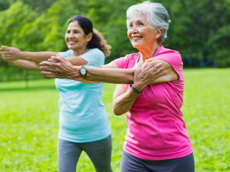 Zwei Frauen machen Dehnübungen im Freien auf einer grünen Wiese.